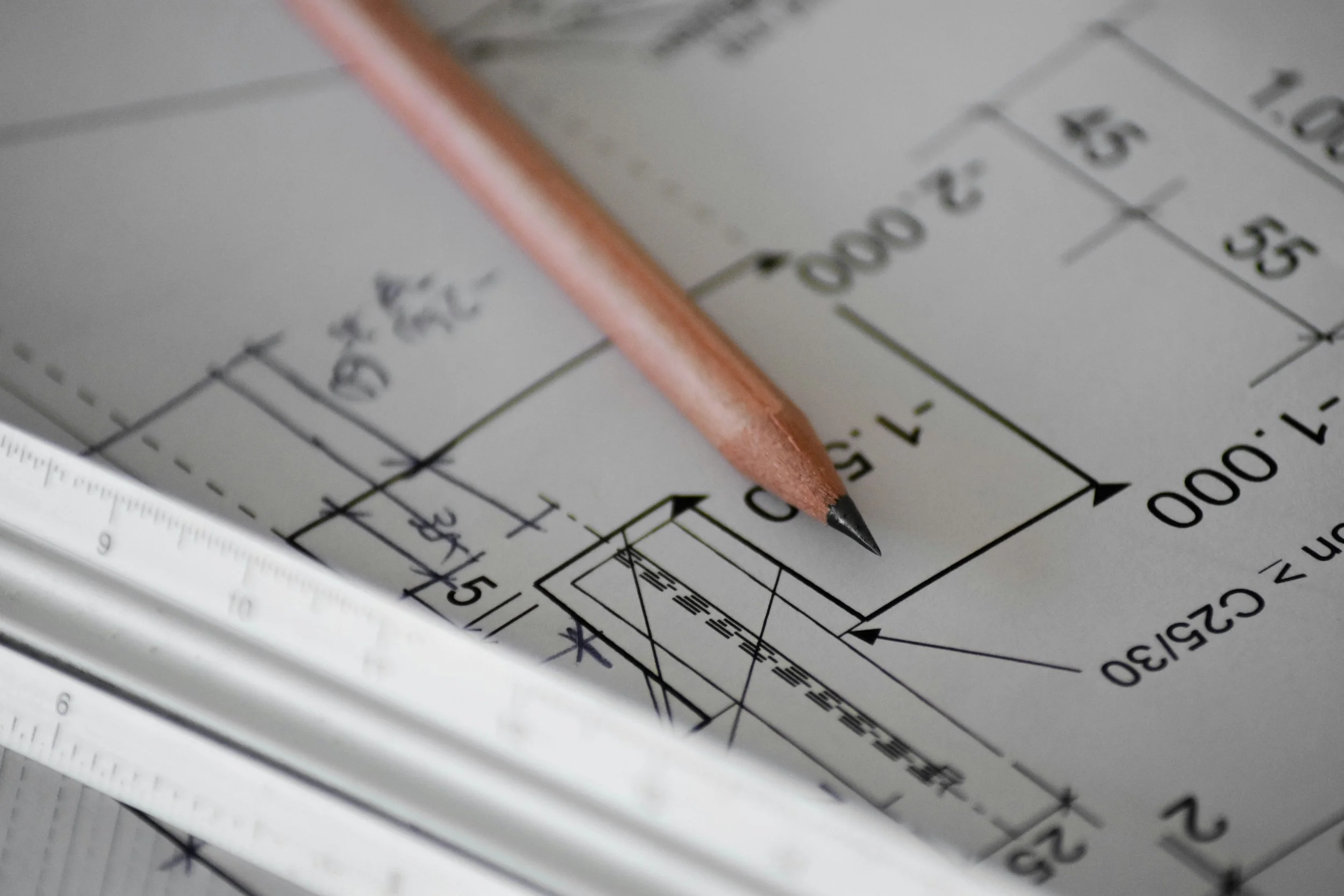 Close-up of a technical drawing or blueprint with a wooden pencil and a white scale ruler on top.