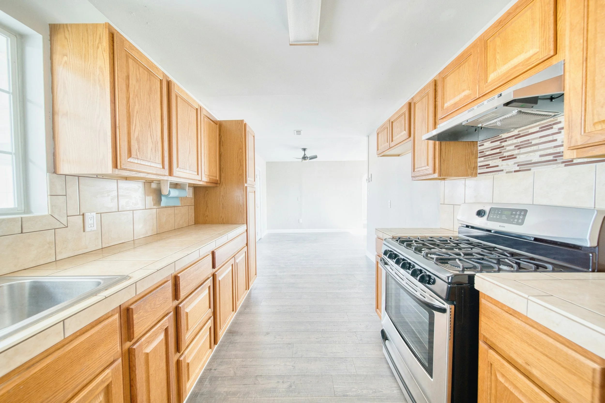 Bright kitchen with wooden cabinets, beige tiled countertops, stainless steel stove, and window with natural light.
