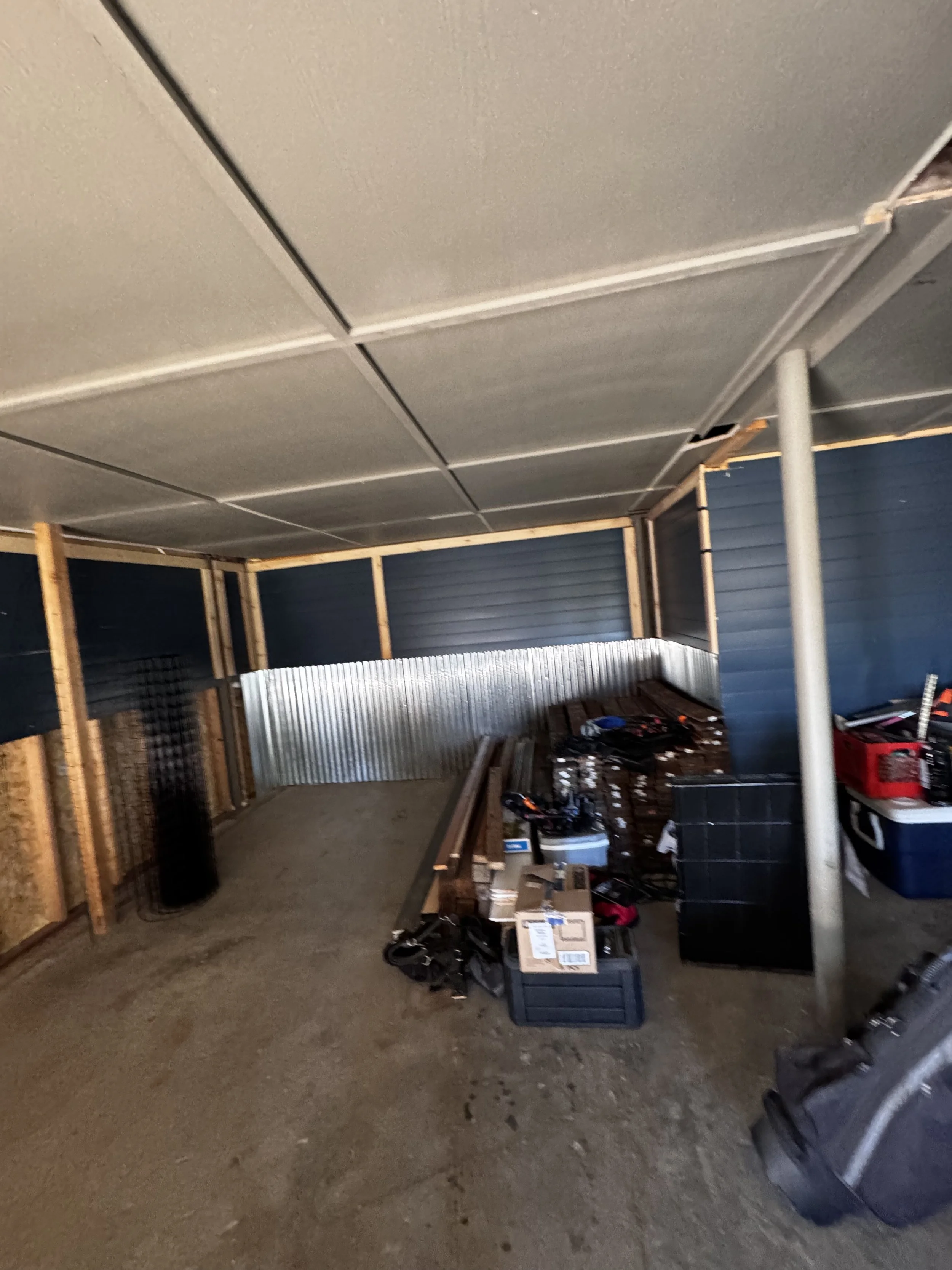 Partially enclosed outdoor space under construction with scattered tools and materials, including wood planks, cardboard boxes, and storage bins.
