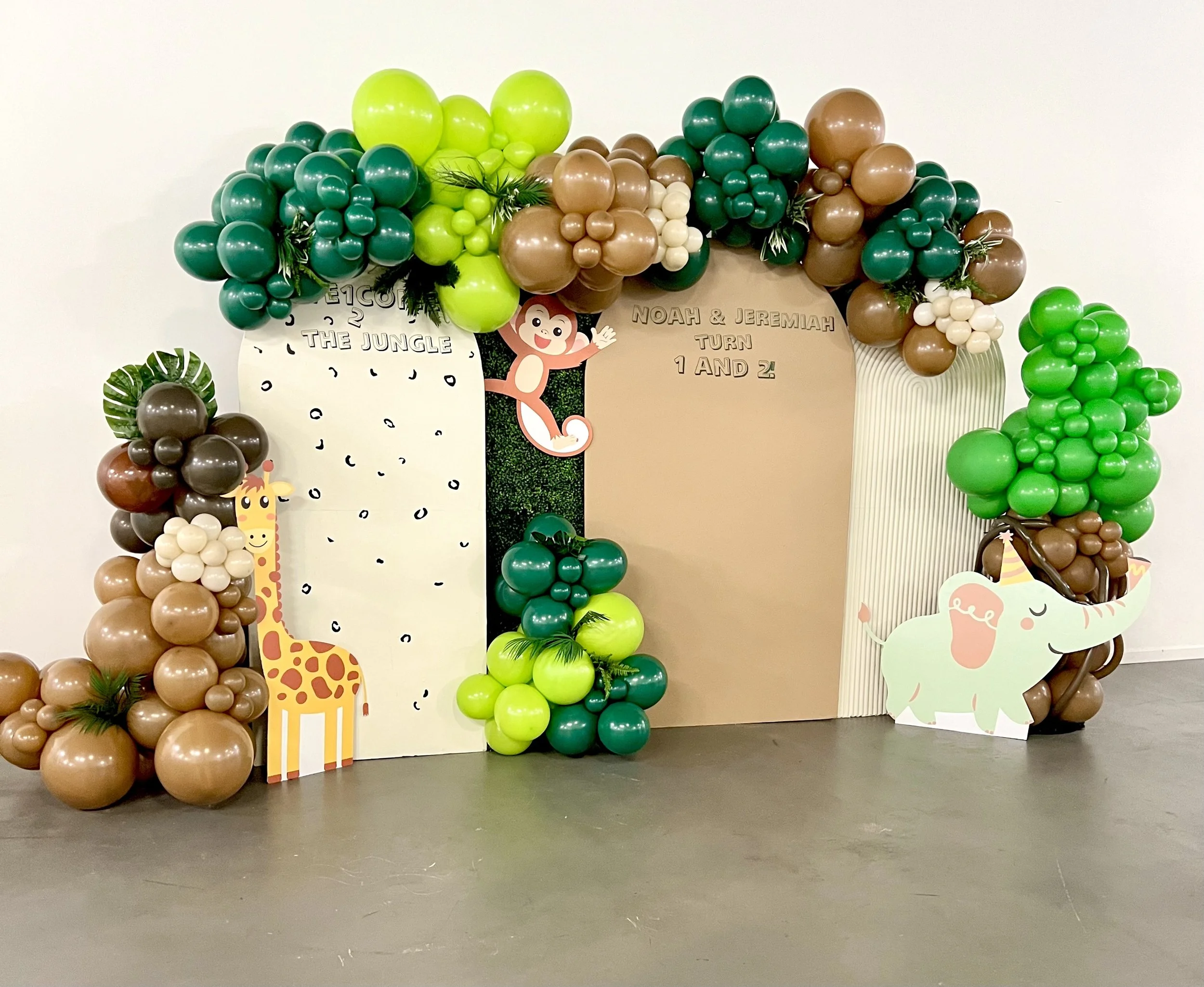 Decorative jungle-themed balloon arch with animals and a sign for Noah and Jeremiah's first birthday celebration.
