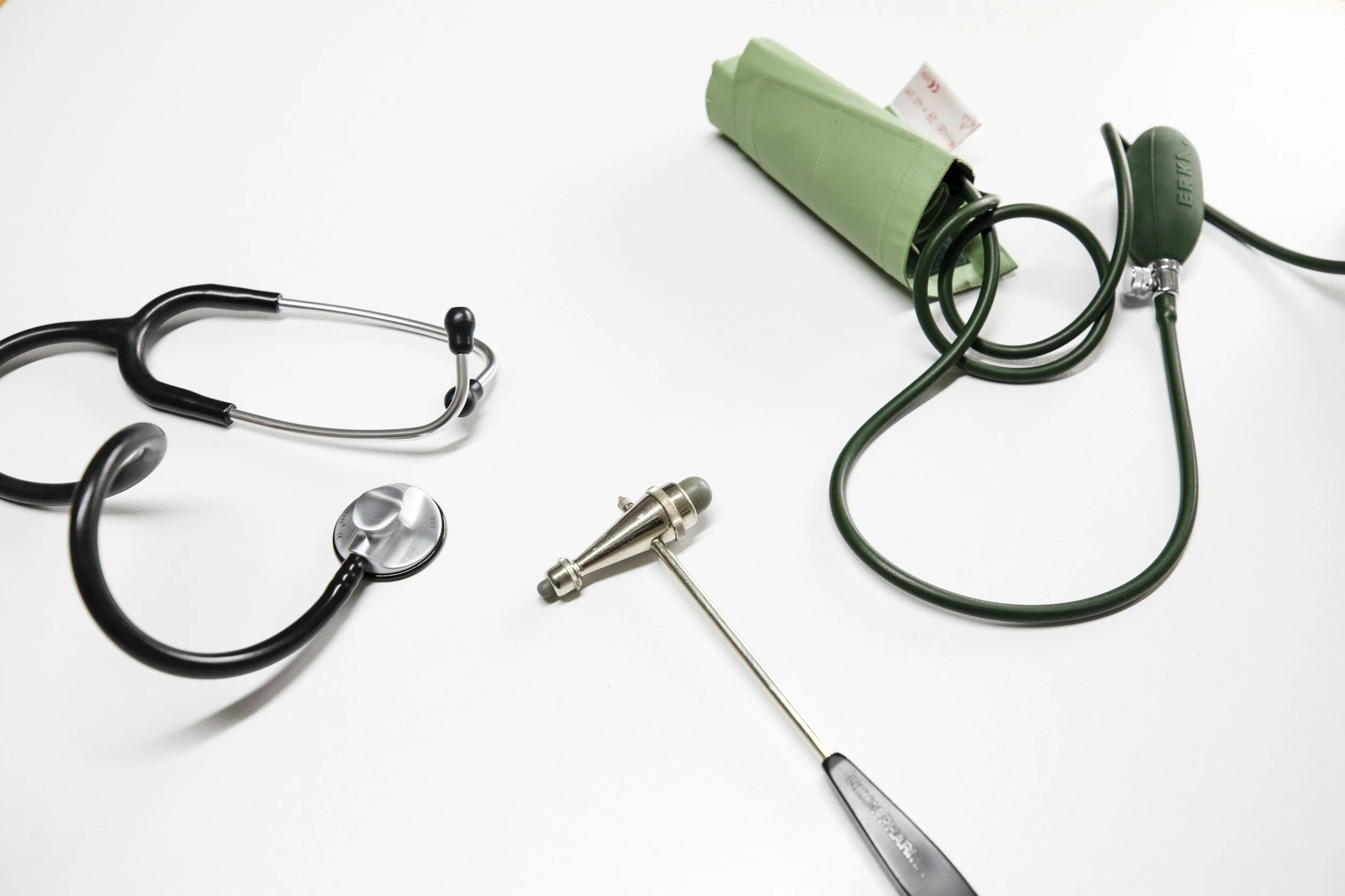 Medical equipment on a white surface including a stethoscope, blood pressure cuff, and metal medical instrument.