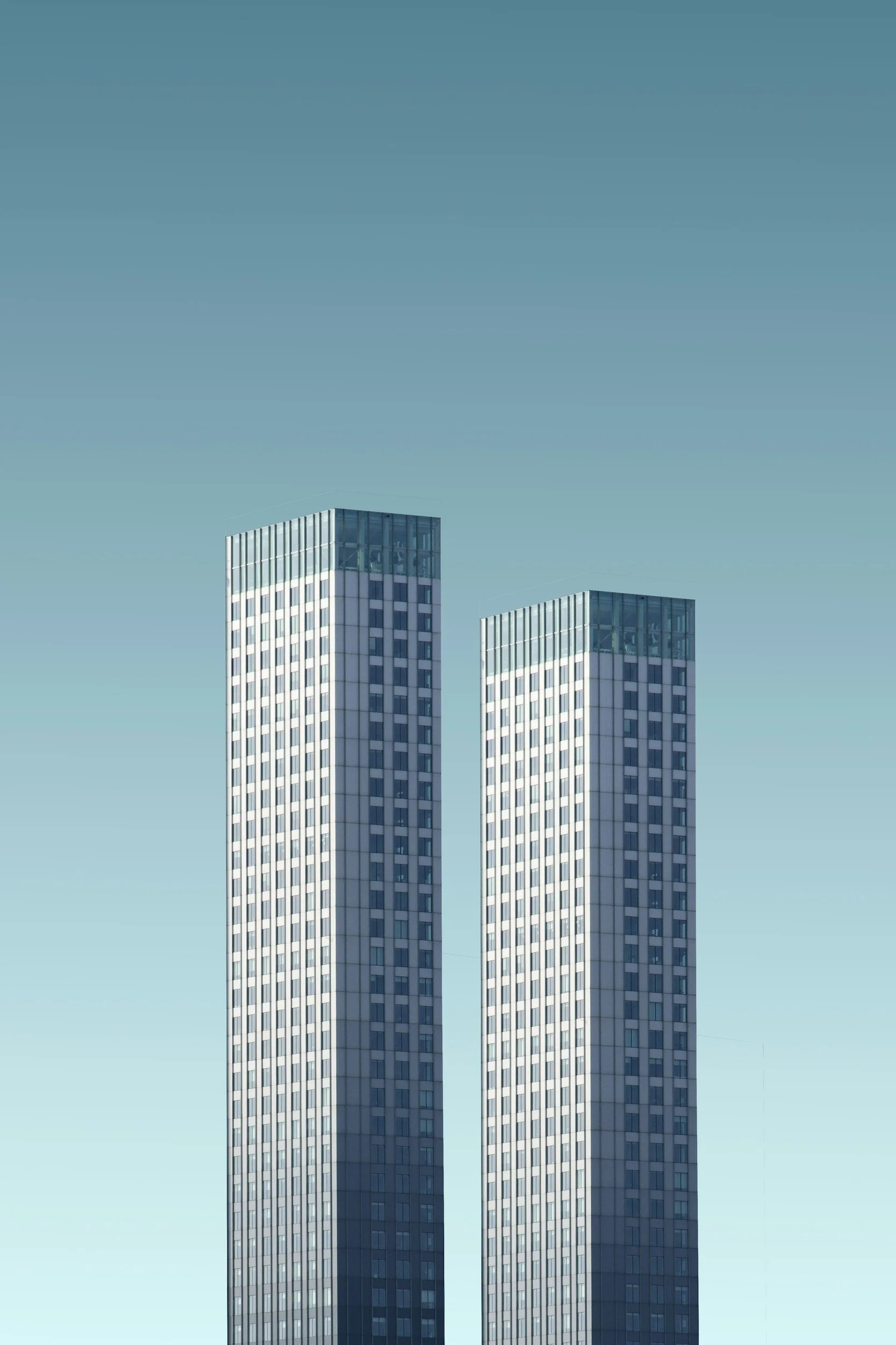 Two tall modern office buildings with glass facades against a clear blue sky.
