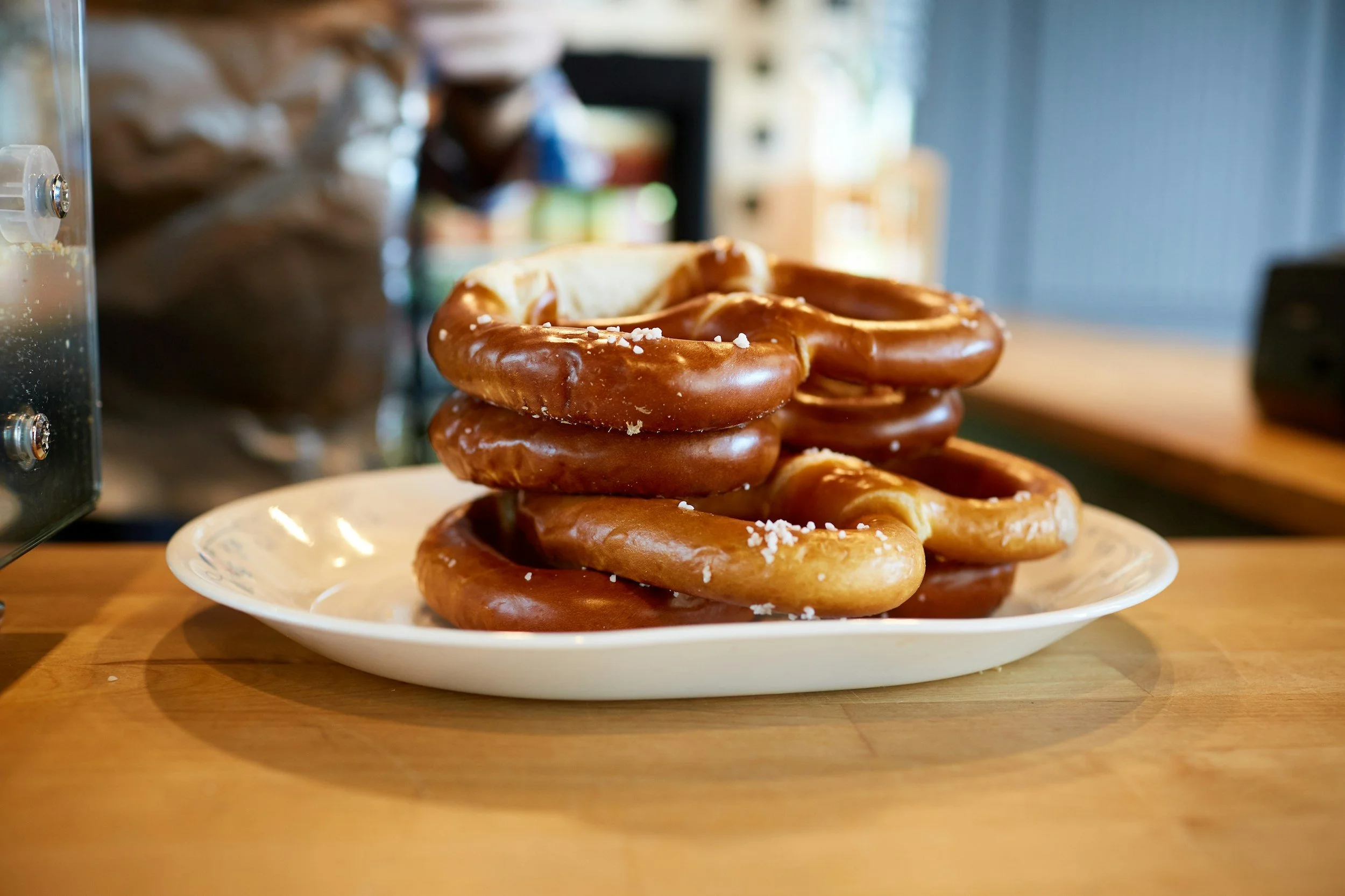 A white plate piled with chocolate-glazed pretzels topped with coarse salt, placed on a wooden table.
