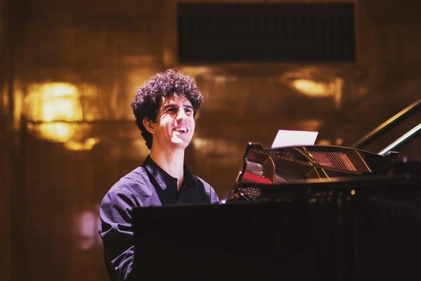 Musician Tim Mallis playing a black grand piano in a dimly lit room.
