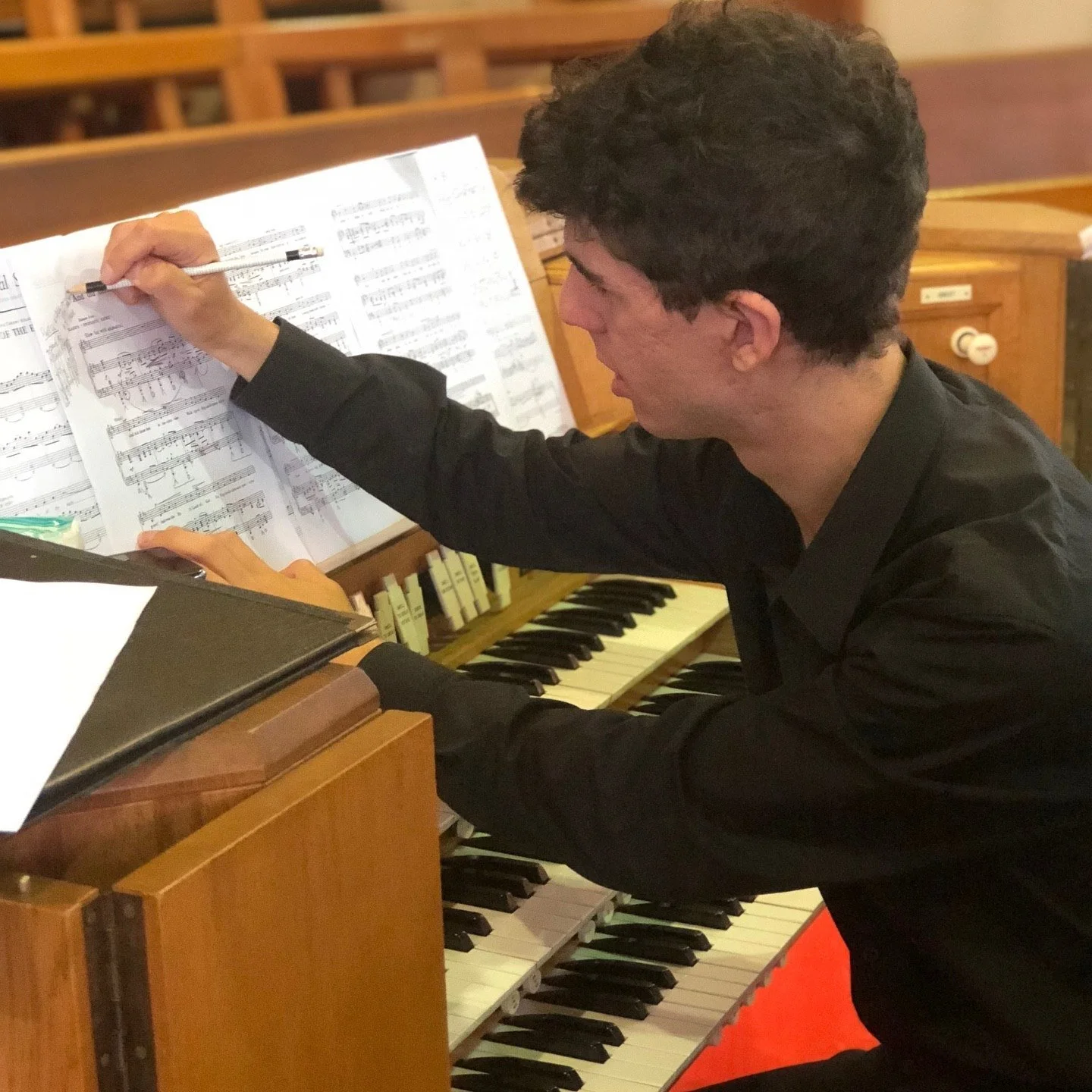Musician Tim Mallis playing the piano with sheet music on the music stand in front of him.