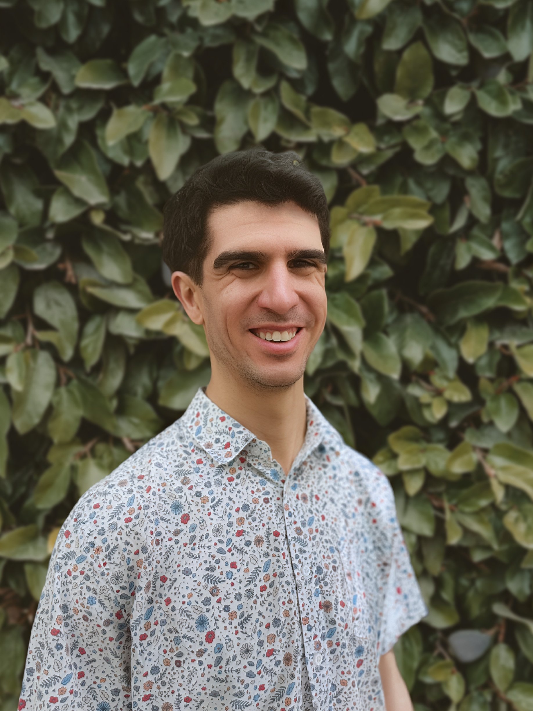 Headshot of musician Tim Mallis in front of a leafy background.