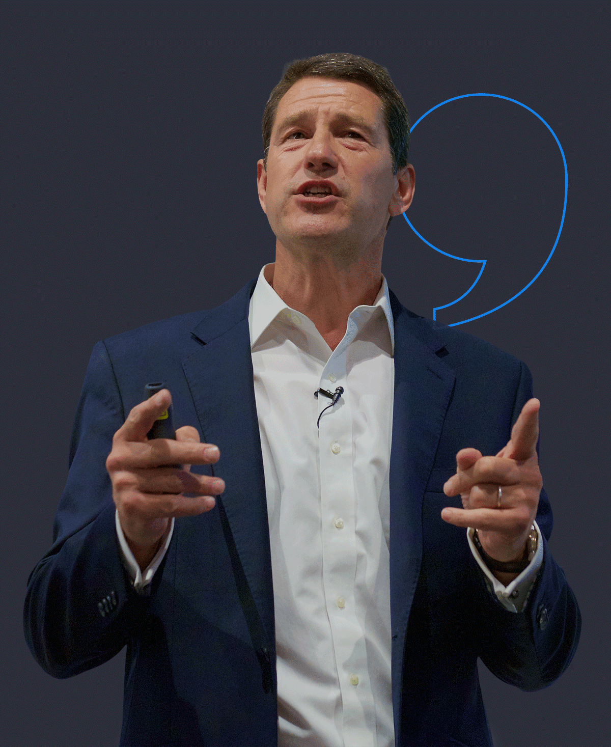 Nick Saunders in a dark blue suit and white shirt speaking, pointing with both hands, with a gray background and a blue speech bubble graphic behind him.