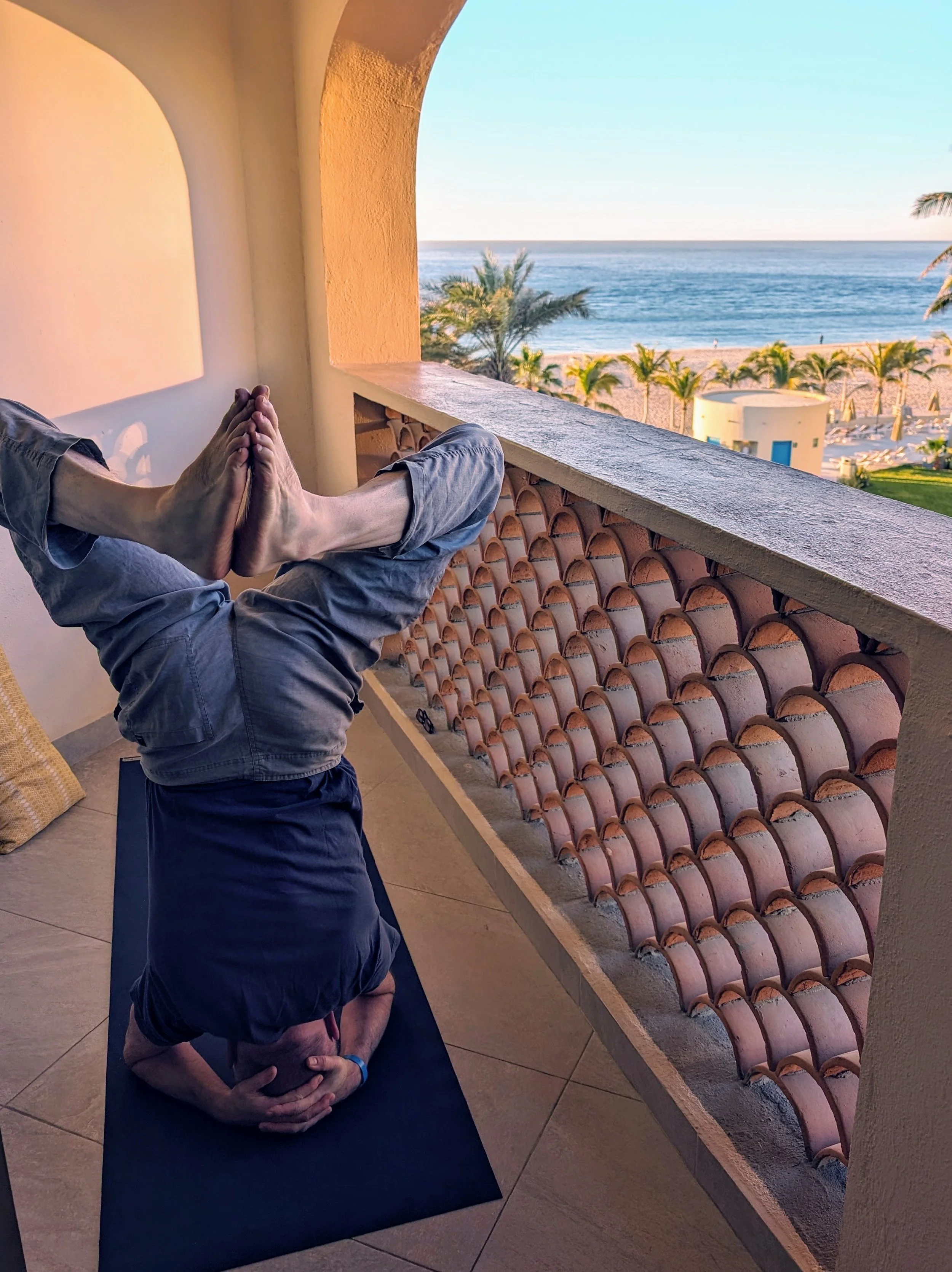 Man standing on his head on a balcony over the sea