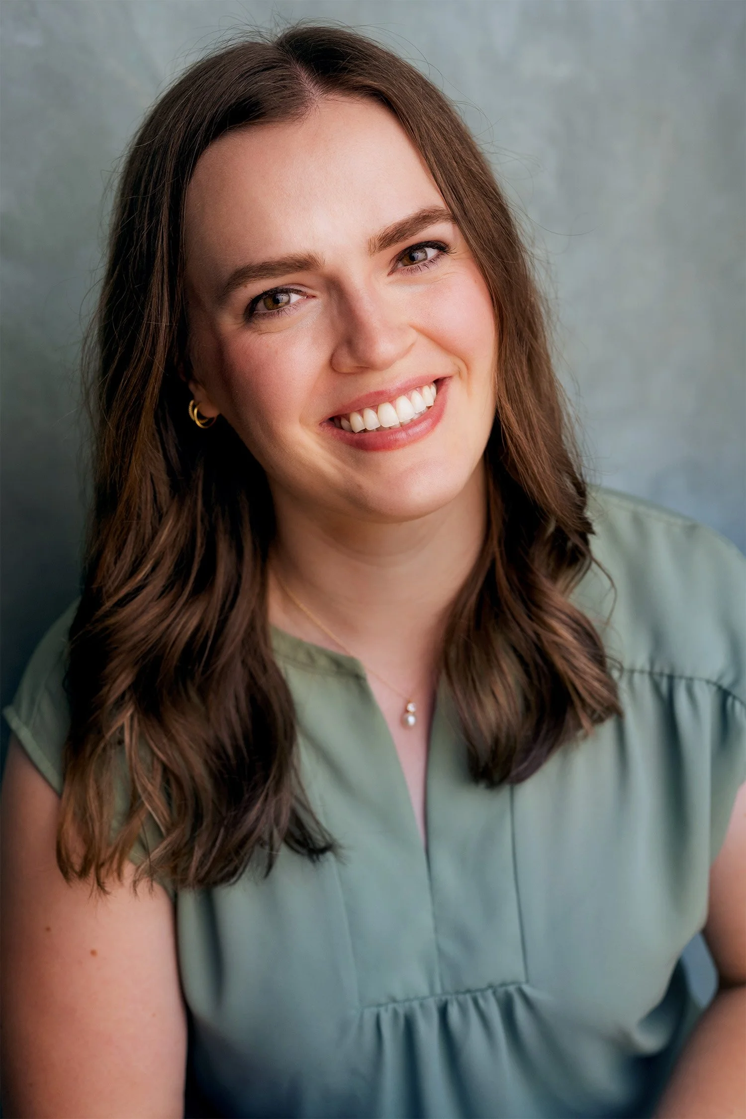 Portrait of Caitlin Moore, a young, white woman with brown hair, smiling, wearing a light green blouse, against a soft gray background.