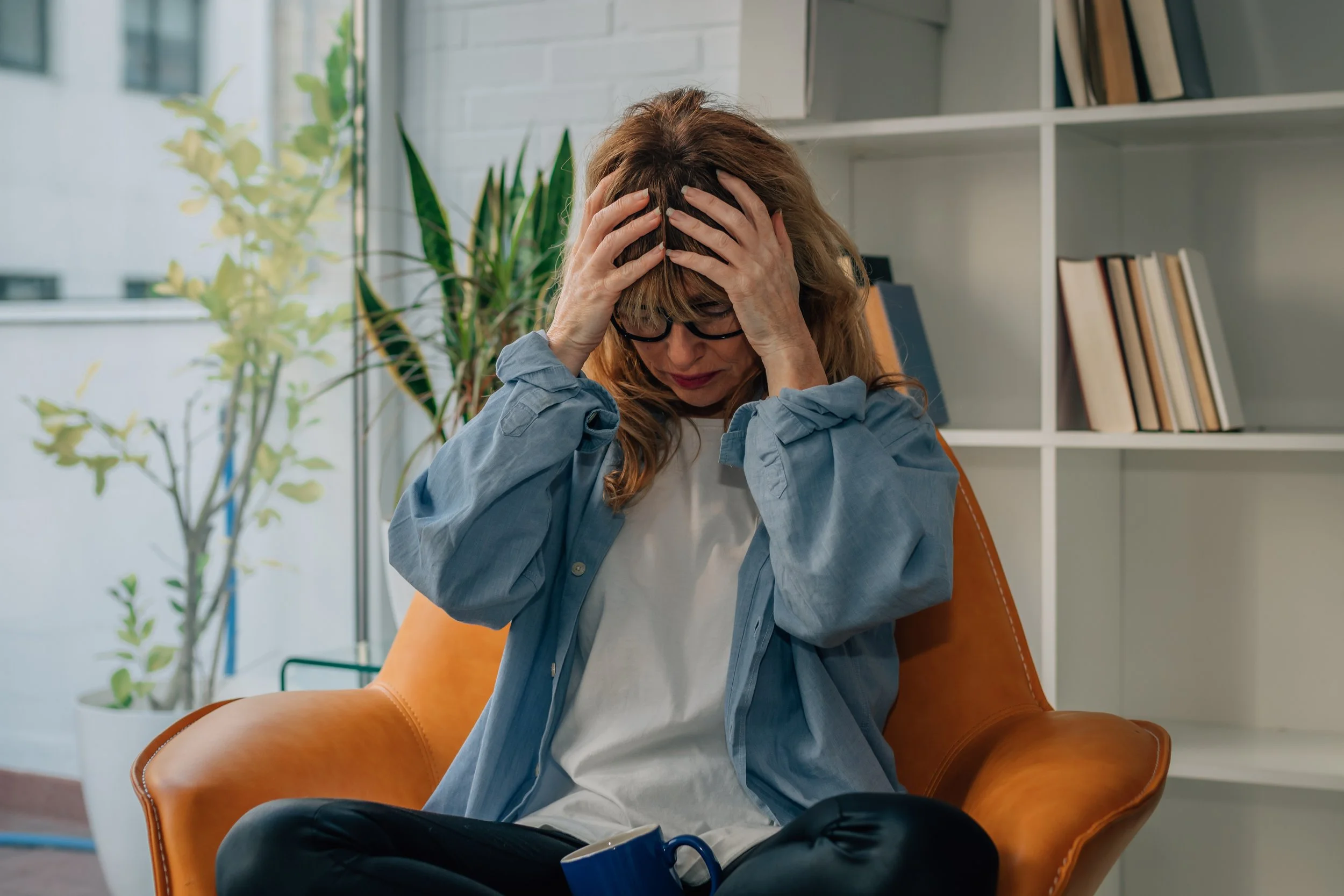 Woman sitting indoors with her hands on her head, appearing overwhelmed.