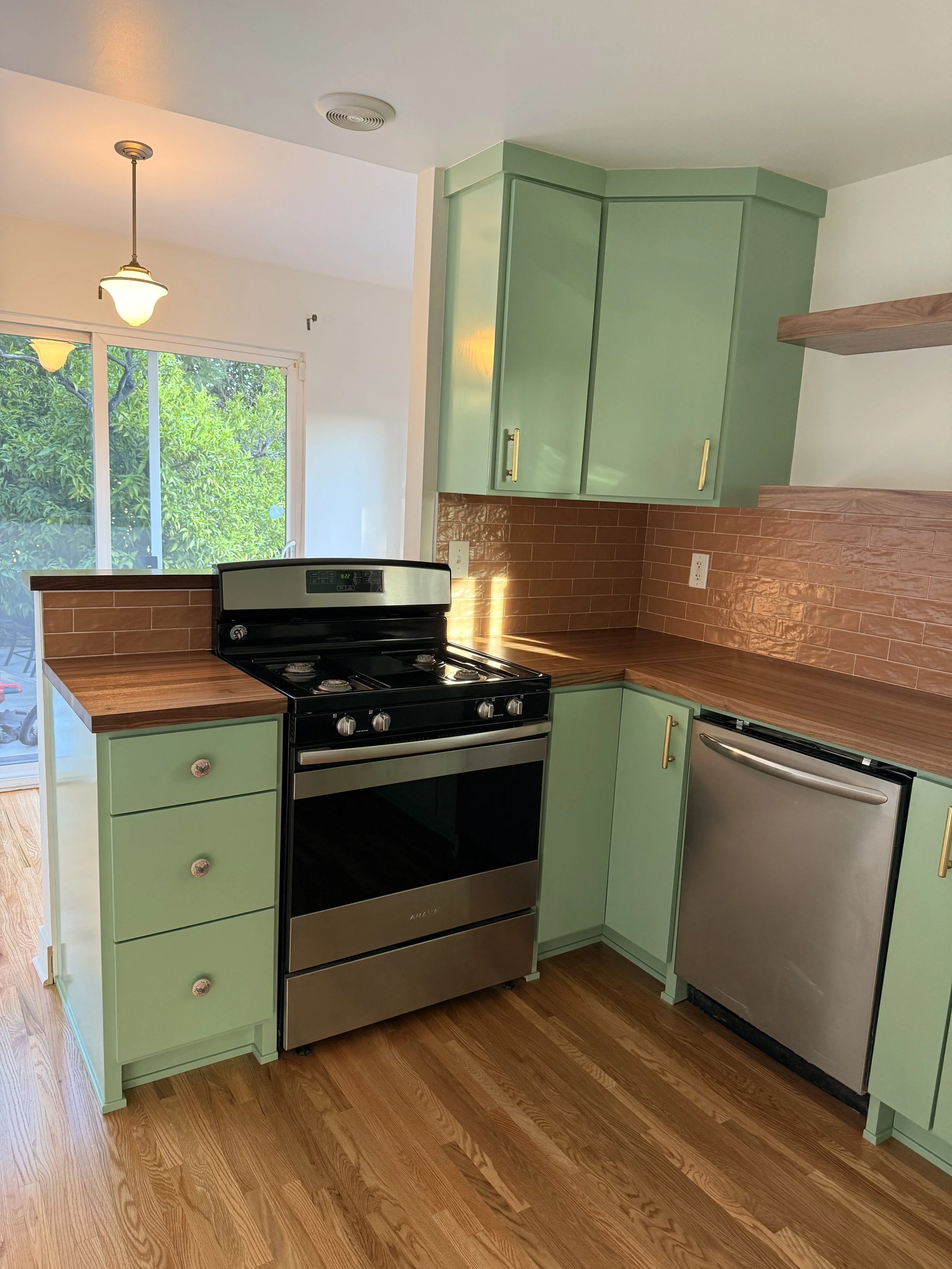 Finished kitchen remodel showing stove wall, custom cabinetry, wood counters, stainless steel dishwasher, and brick-look backsplash.