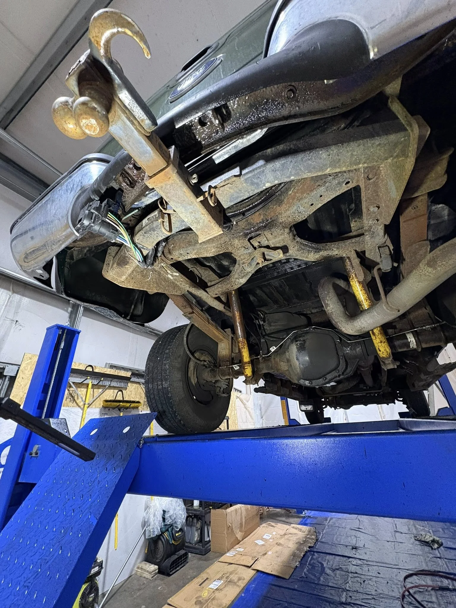 Underside of a vehicle on a blue lift inside IRONCLAD Vehicle Undercoating's indoor workshop.