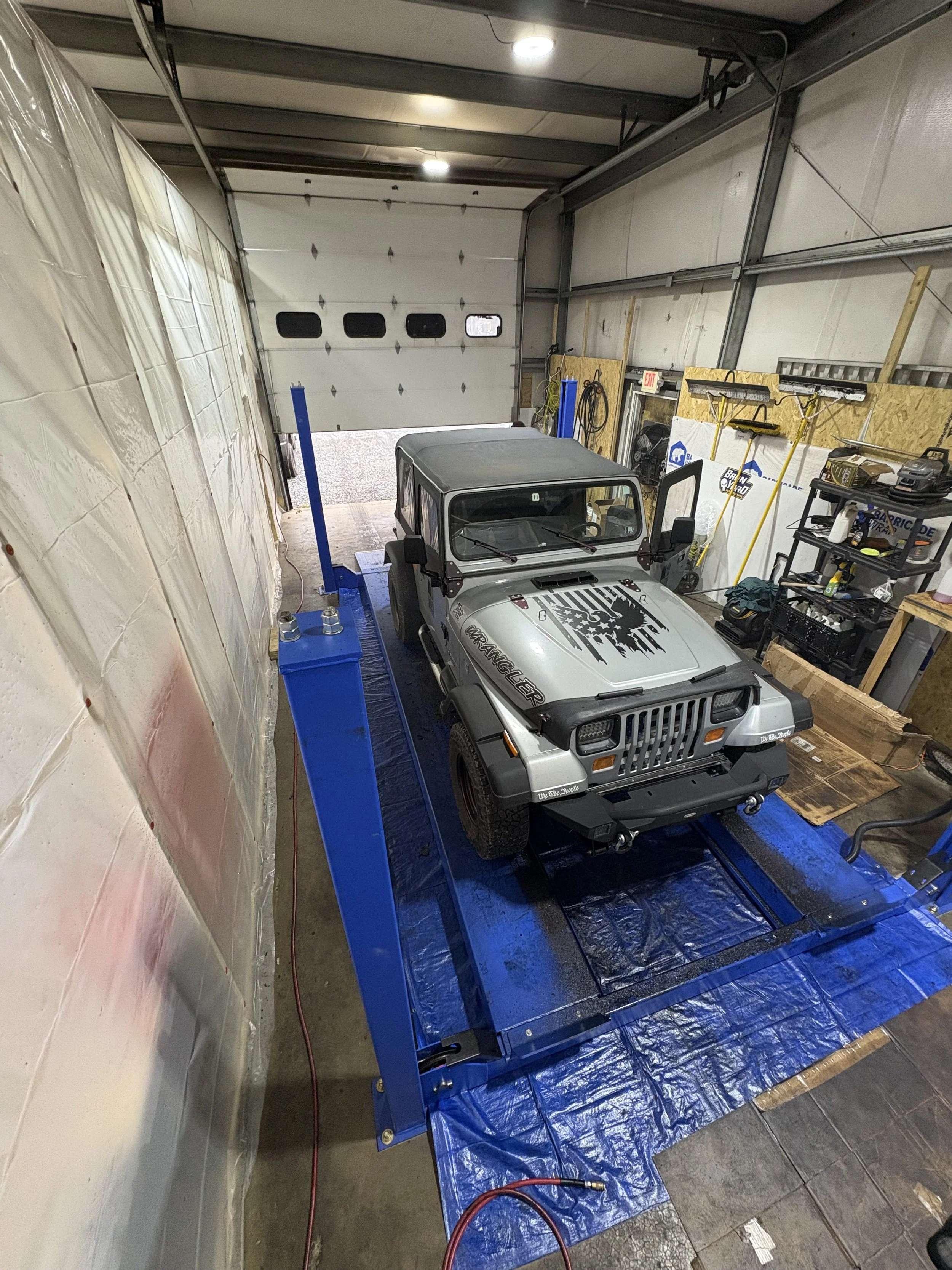 A silver Jeep Wrangler vehicle on a blue lifting platform inside IRONCLAD Vehicle Undercoating's indoor workshop.