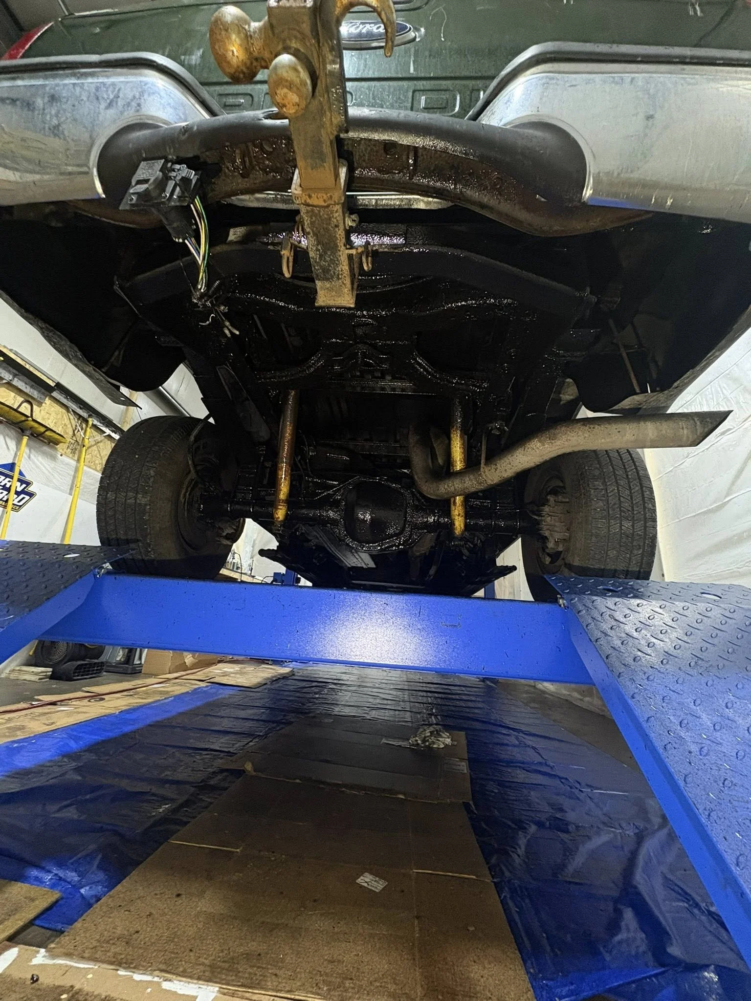 Undercarriage of a pickup truck on a lift after fresh IRONCLAD undercoating application, showing full rust-protection coverage.