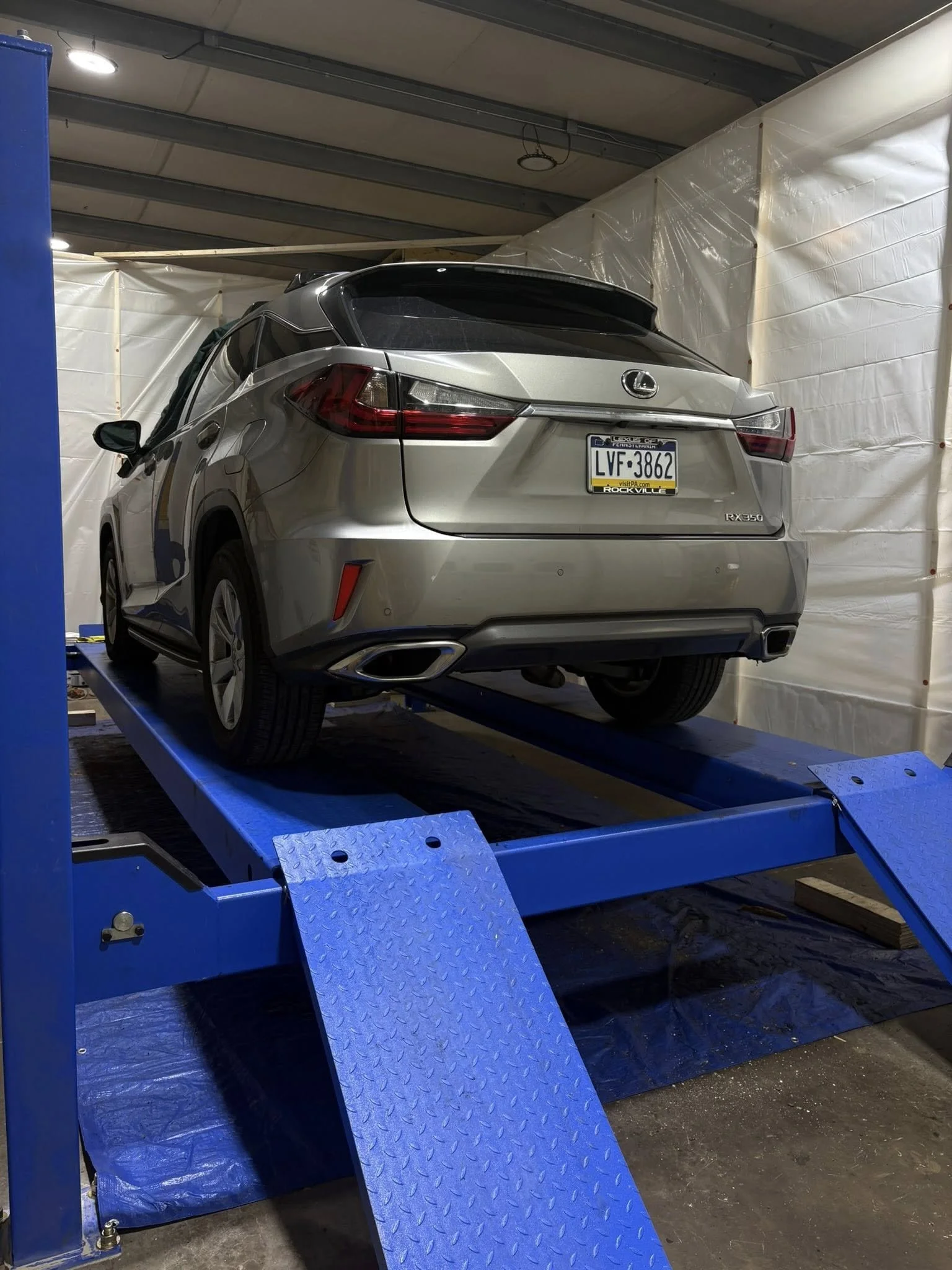 A silver Lexus RX 350 SUV on a blue vehicle lift in IRONCLAD Vehicle Undercoating's indoor workshop.
