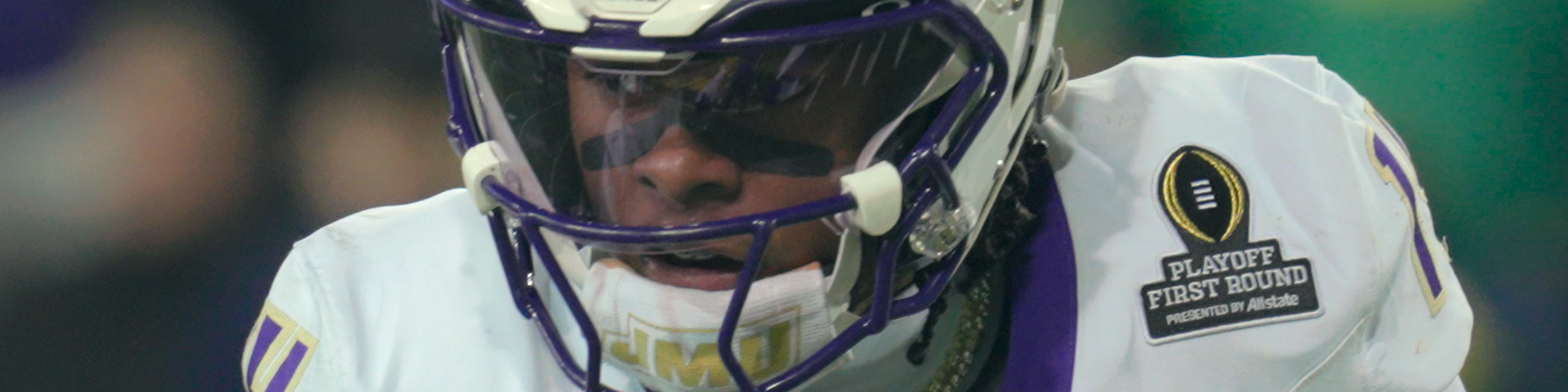 Close-up of a football player wearing a purple and white uniform with a helmet and visor, during a game.