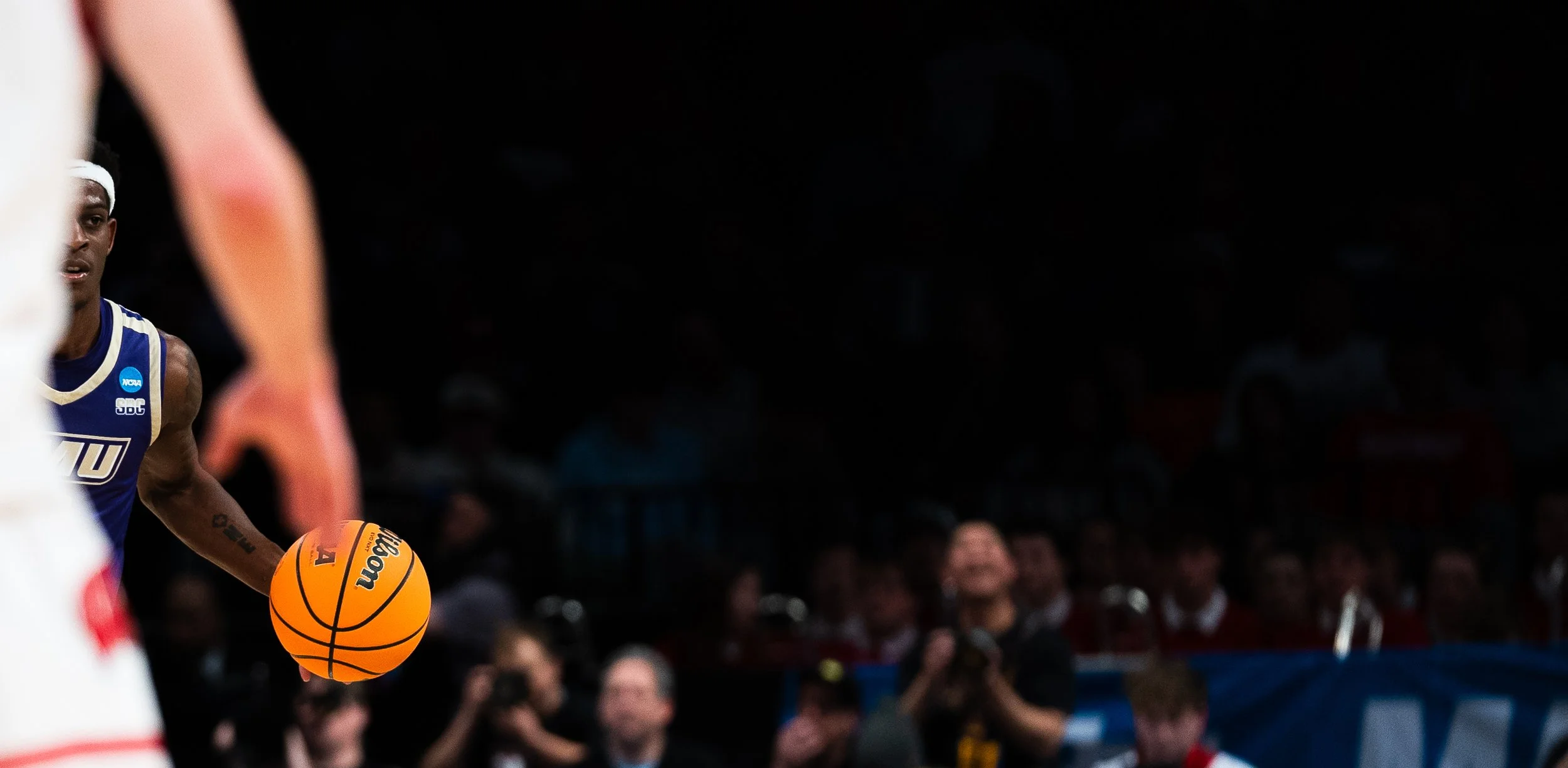 Basketball player in a blue uniform holding an orange basketball during a game, with spectators in the background.