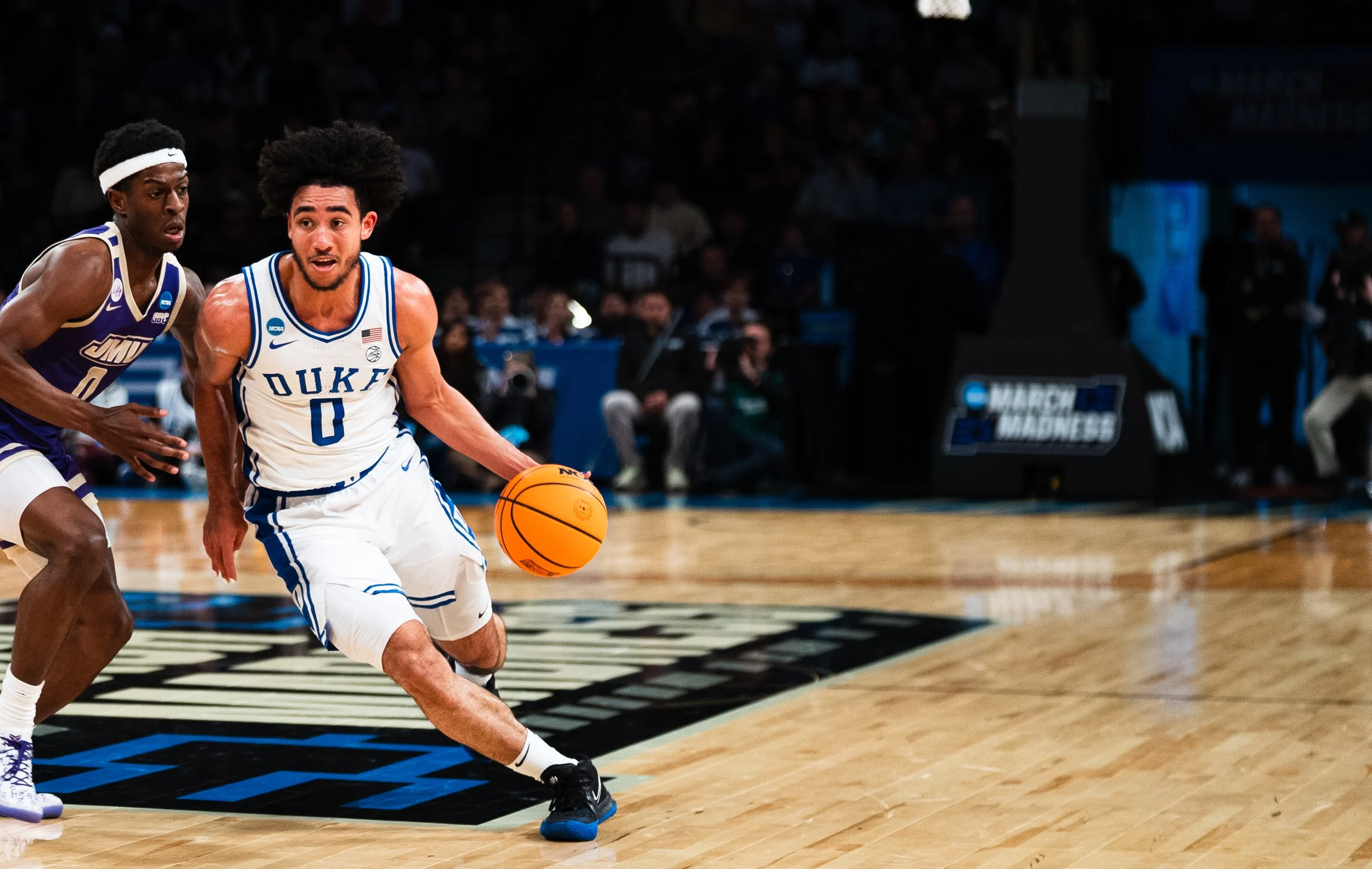 College basketball game: player from Duke attempting to dribble the ball while being guarded by a player from James Madison.