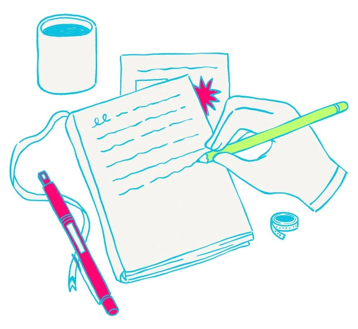A hand writing in a notebook with a yellow pen, a red and gray pen beside it, a mug, a photograph or card with a pink starburst, and a small rolled piece of paper or tape on a desk.
