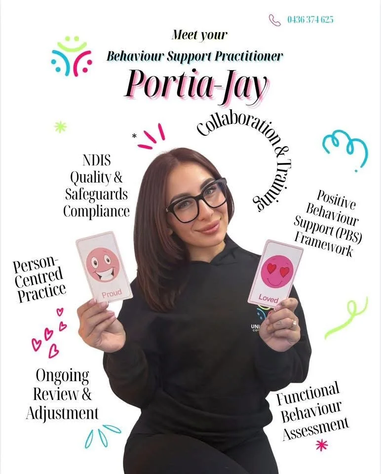 A woman with shoulder-length brown hair, wearing glasses and a black shirt, is holding two cards with smiley face illustrations. The card in her left hand shows a happy face labeled 'Proud,' and the card in her right hand shows a loved face labeled 'Loved.' There are colorful decorative elements and text highlighting her role as a Behaviour Support Practitioner, mentioning collaboration, training, and assessment.