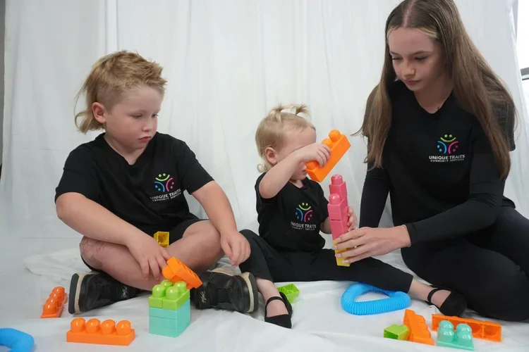 Three children and a woman sitting on the floor playing with colorful building blocks and toys.