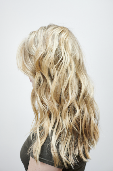 Blonde woman with wavy hair facing sideways against a light gray background.