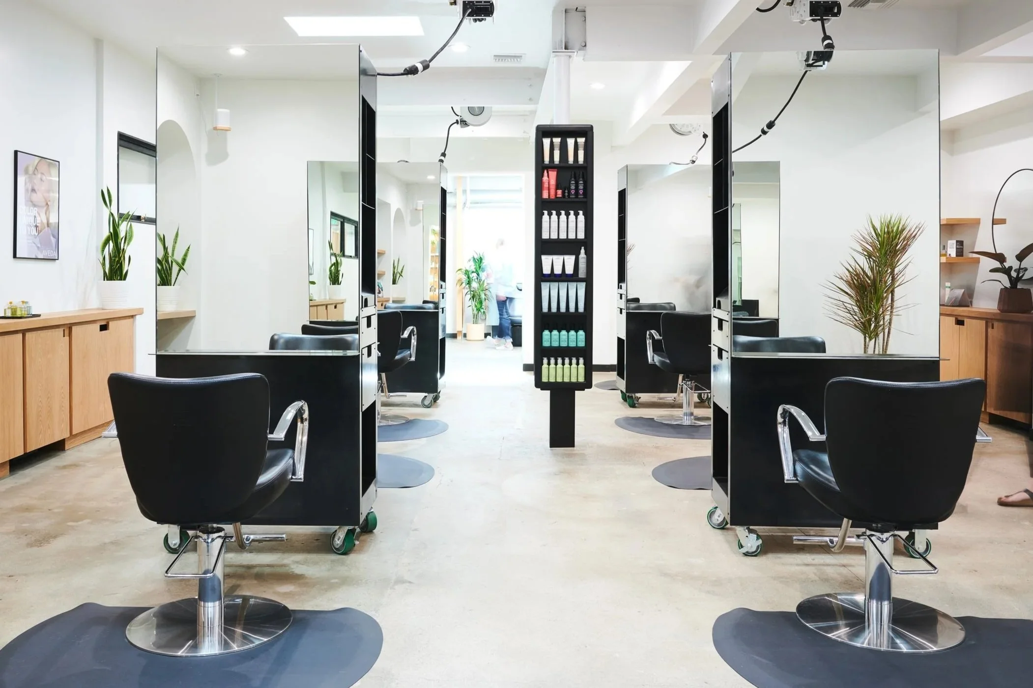 Modern hair salon with black styling chairs, mirrors, and hair product shelves in a bright space with white walls and wooden accents.