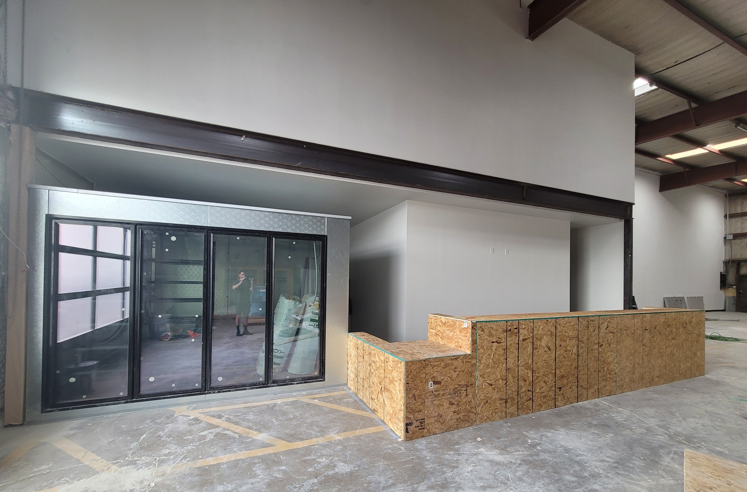 Construction site with a partially finished interior space, including a glass wall with black frames, wooden structures, and an open floor area with construction materials.