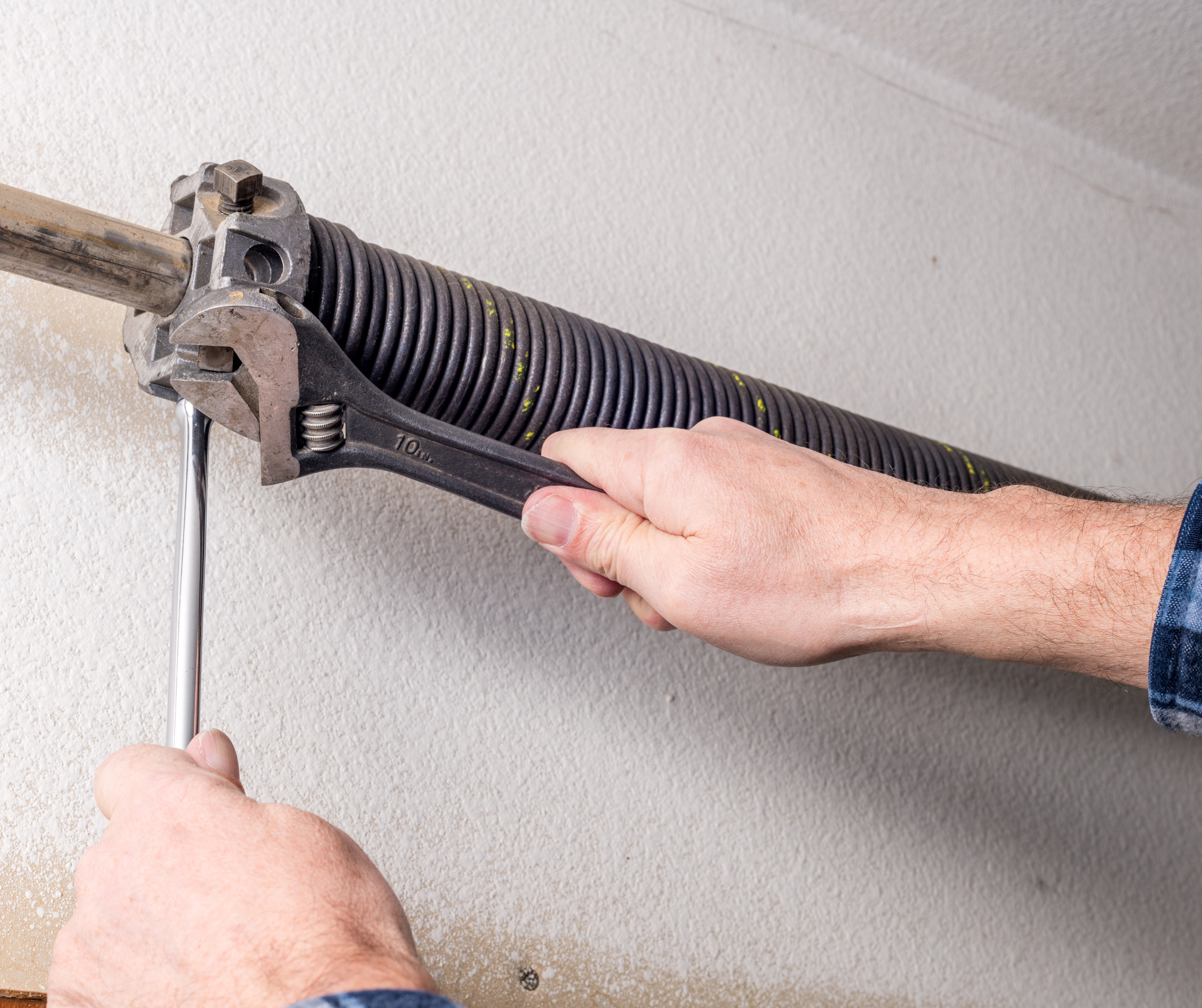 A person installing or repairing a flexible conduit on a wall using a wrench and a screwdriver.