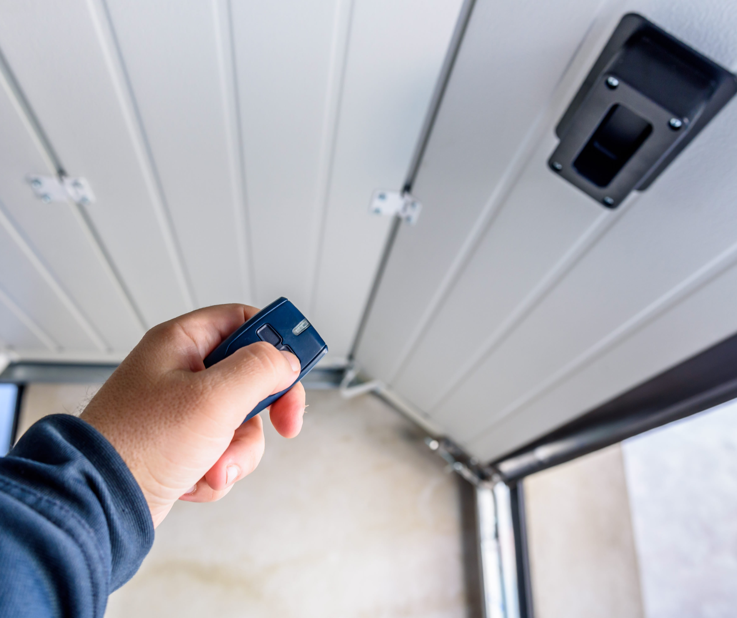 A person holding a remote control towards a garage door sensor on a garage door.