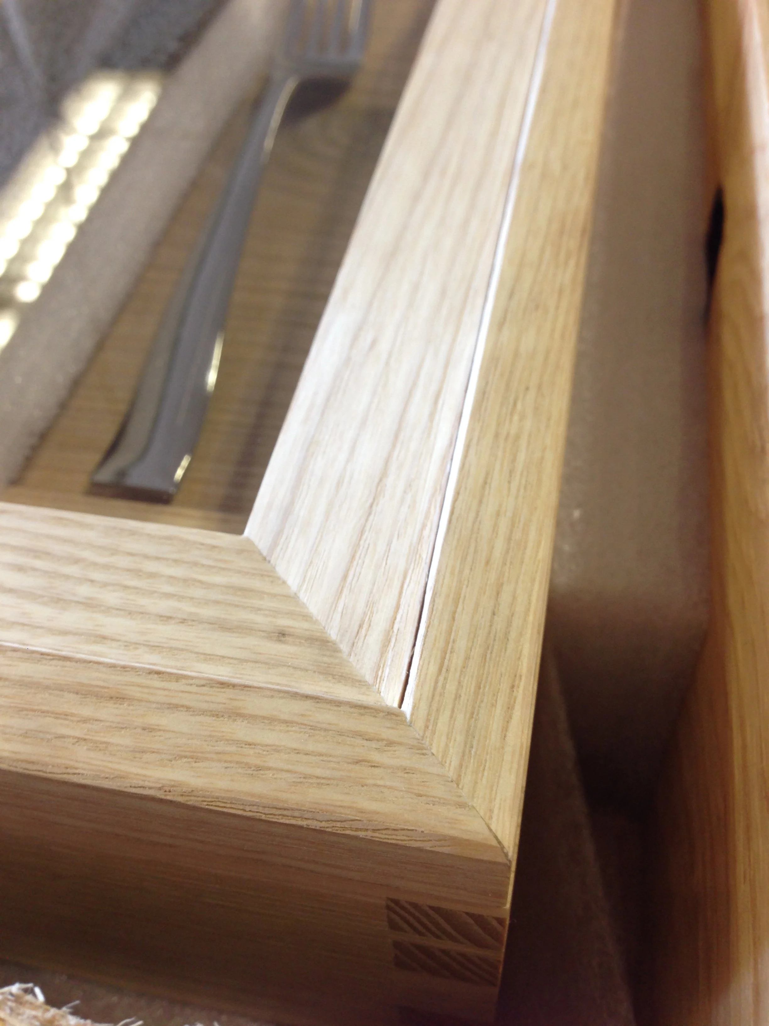 Close-up view of a wooden framed display case with a glass top, showing a corner with beveled edges and a visible wood grain.