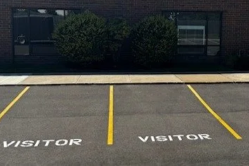 Empty parking lot with yellow lines and the word 'VISITOR' painted on the ground.