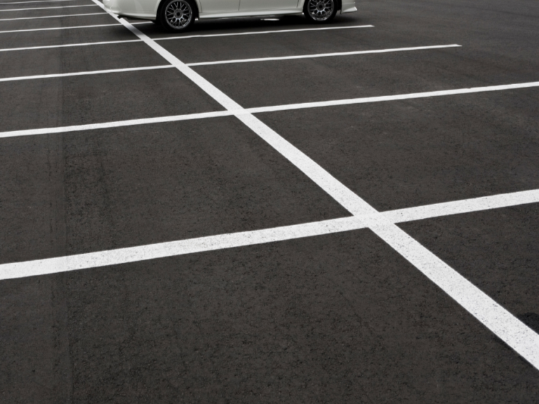 Empty parking lot with white painted parking space lines and a parked silver car in background.