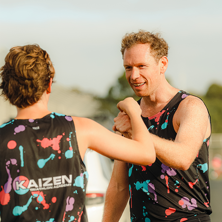 Two smiling men in athletic wear with colorful paint splatters, celebrating a victory or friendship outdoors.
