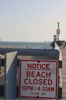 Beach closed sign at the shore with a lighthouse and ocean in the background.