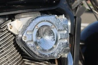Close-up of a motorcycle engine's shiny, round, metallic cover with water droplets on it.