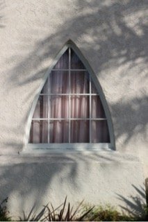 Dormer window in a white stucco wall with shadows of tree branches
