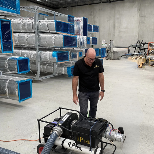 A man inspecting industrial HVAC equipment in a warehouse, with metal ductwork and machinery around him.