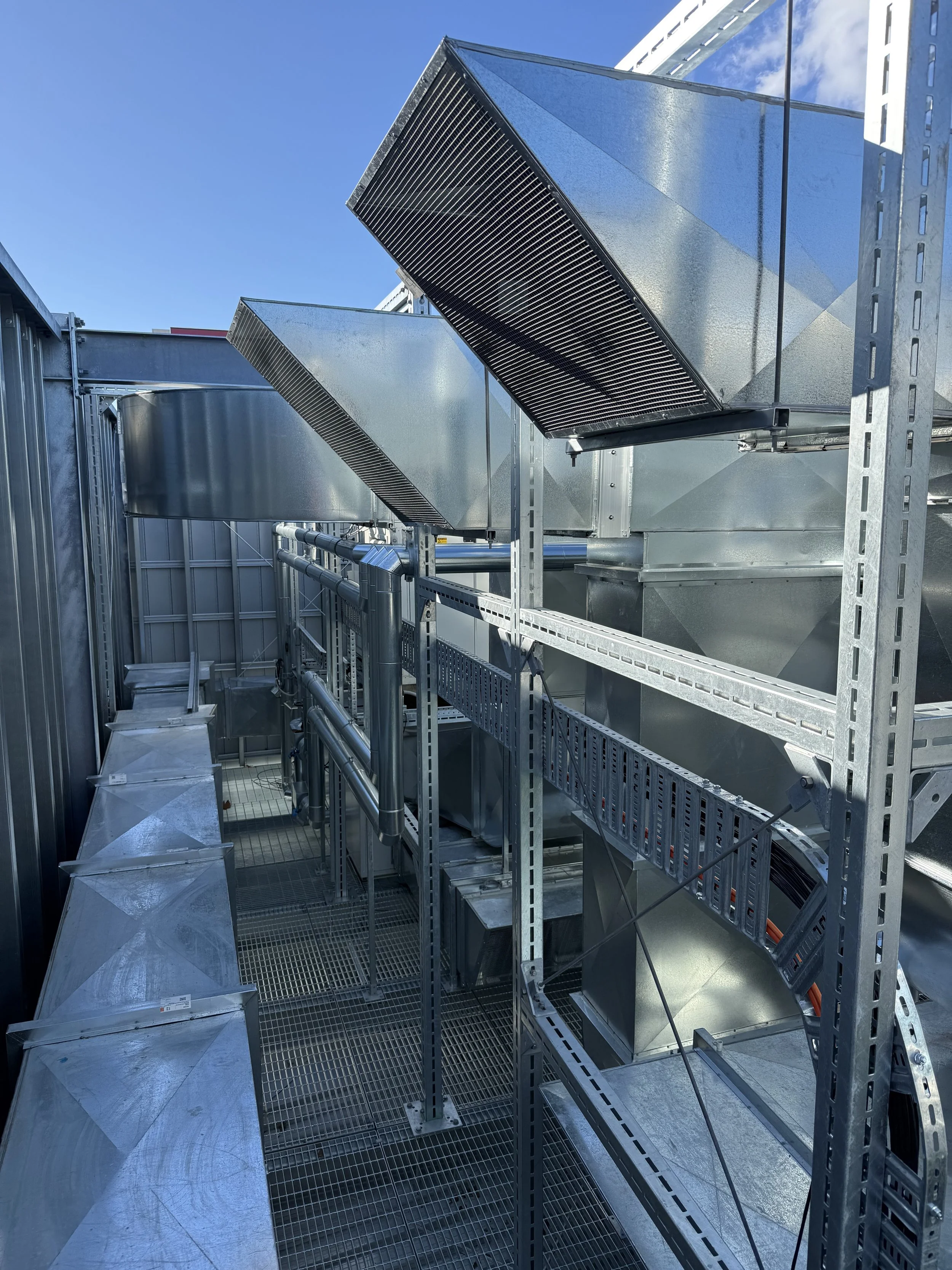 View of industrial HVAC ducting and ventilation equipment on a rooftop with a clear blue sky.