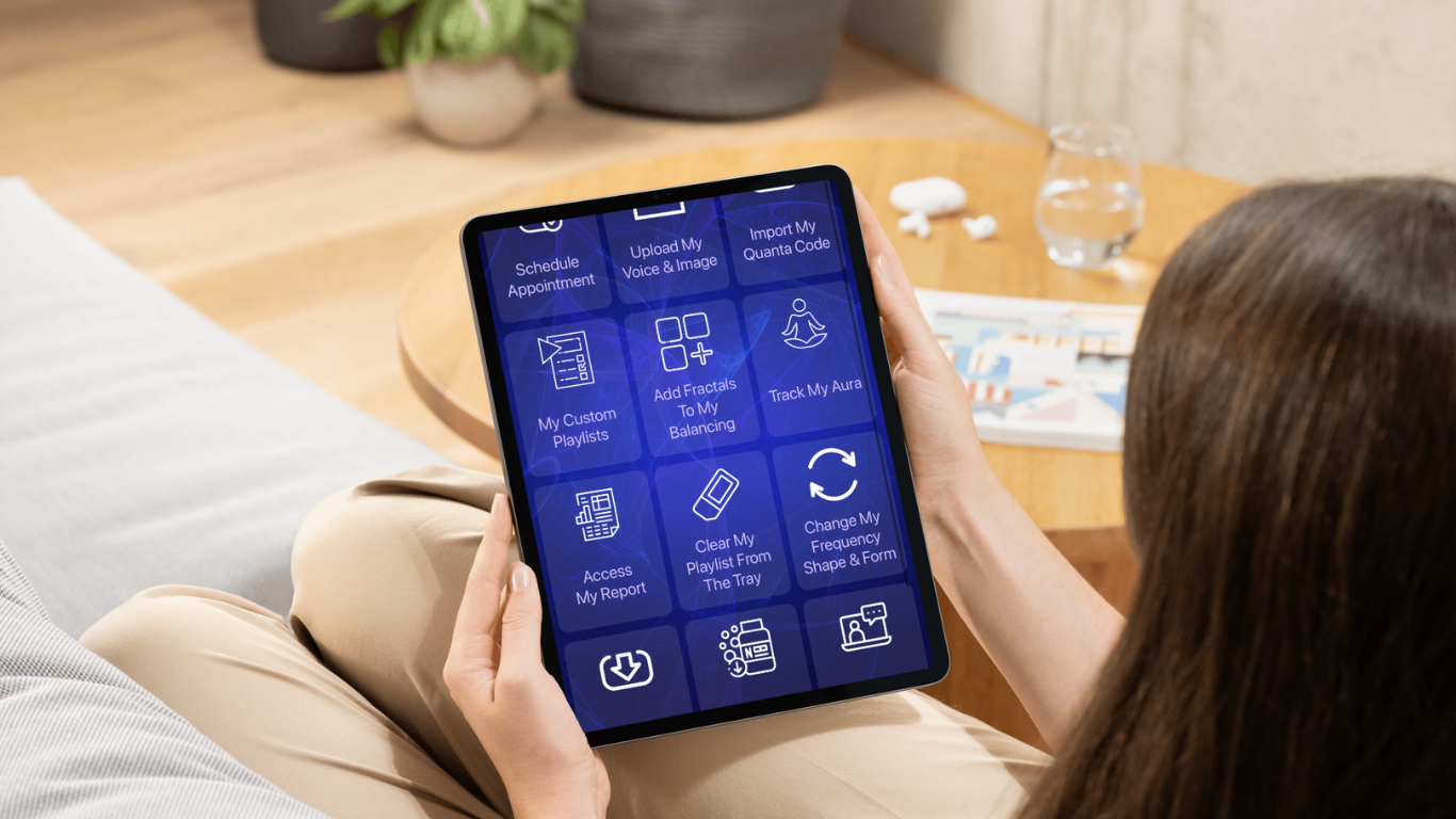 Person holding a tablet displaying a health or meditation app with options for scheduling, playlists, and aura tracking, sitting on a beige couch in a cozy room.