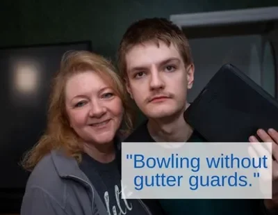 A woman and a young man holding a bowling ball in an indoor bowling alley.