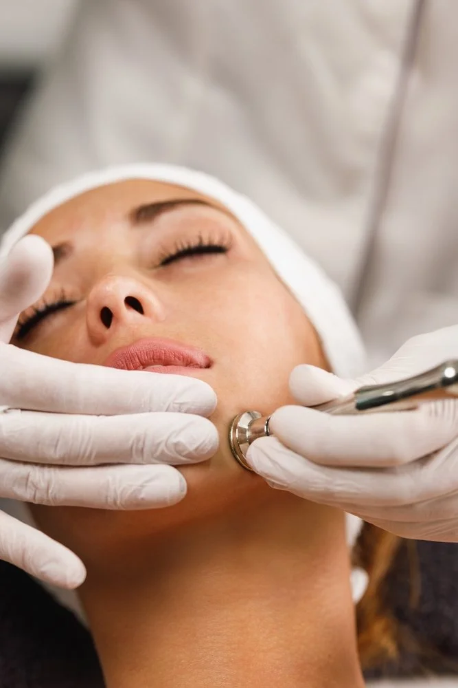 A woman undergoing a cosmetic or medical procedure on her chin, with a healthcare professional handling a medical instrument near her face.