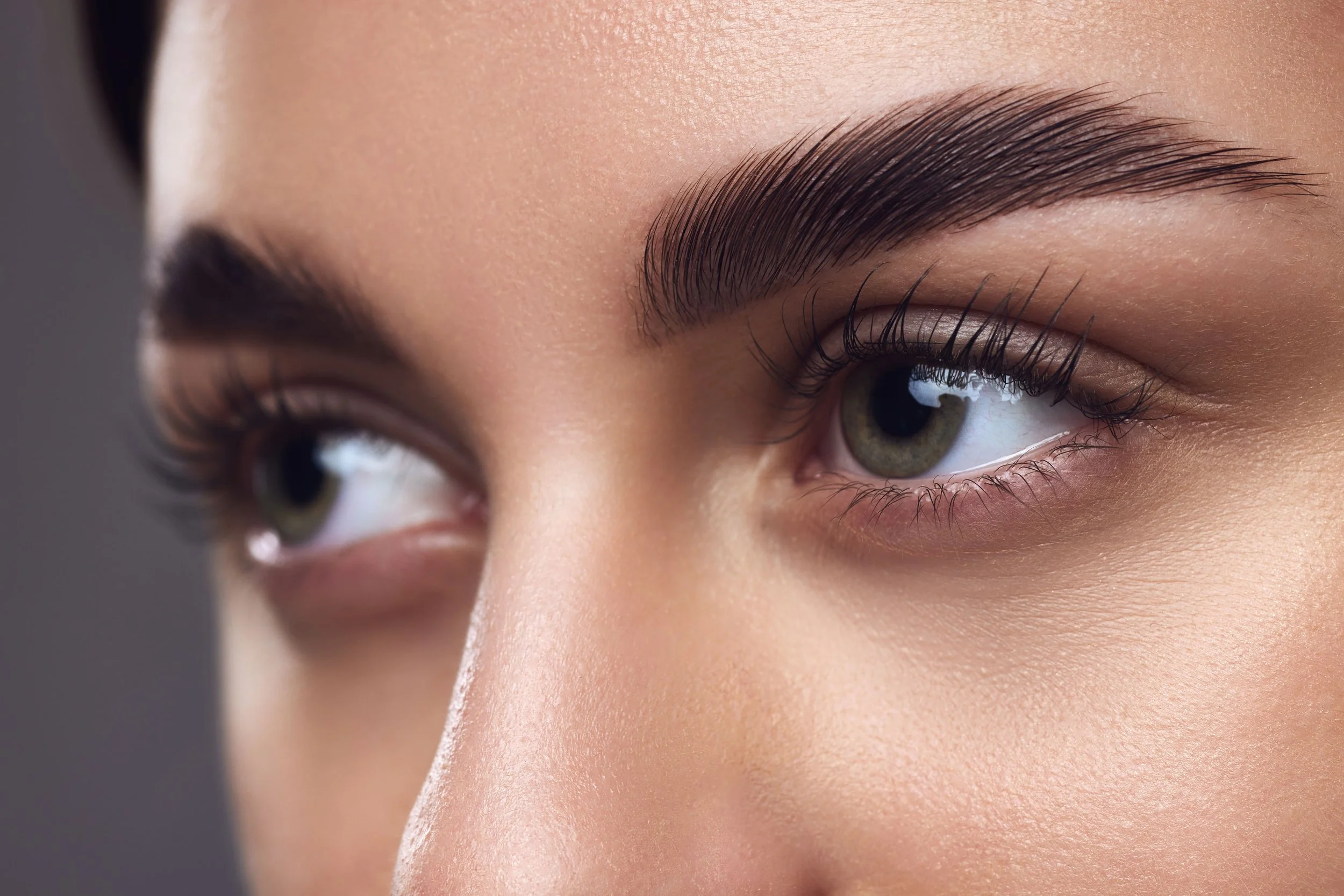 Close-up of a woman's face focusing on her eyes, showing well-groomed eyebrows, long eyelashes, and smooth skin.