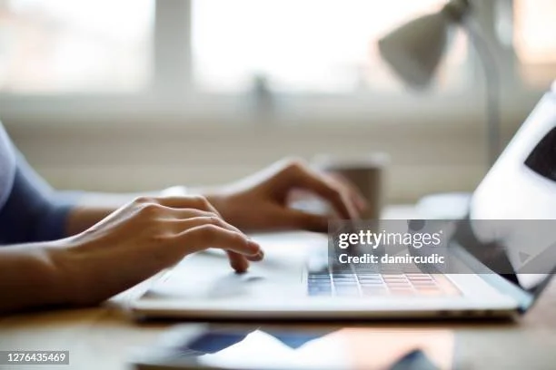 Person typing on a laptop keyboard at a desk with a blurred background.