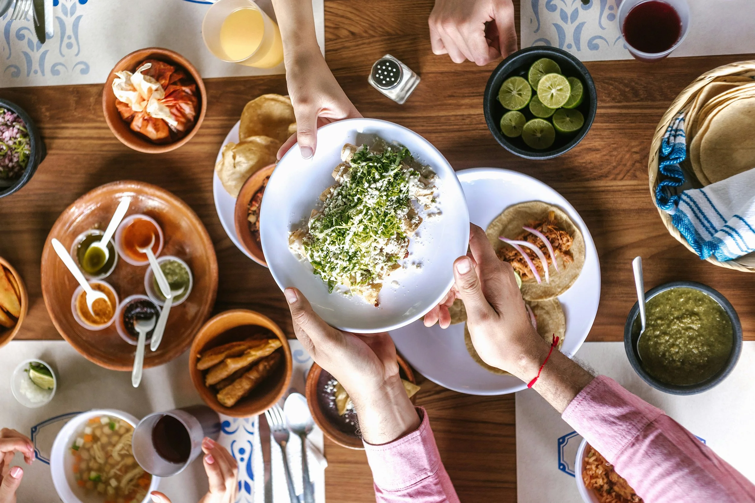 Friends passing plates of tacos and salsa across a shared table
