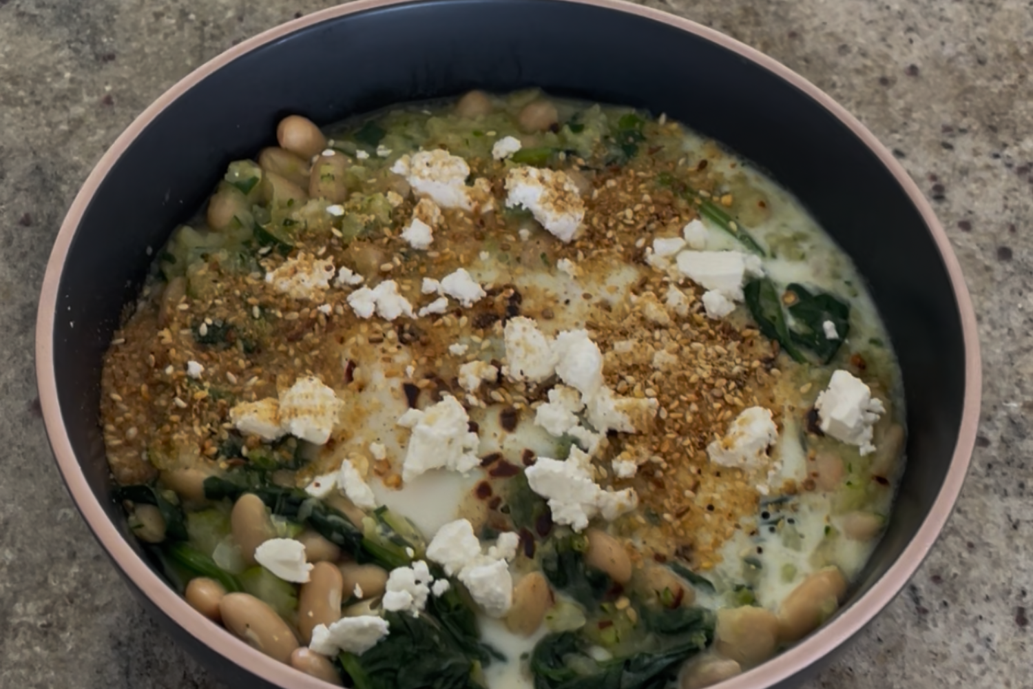 Green Eggs and Gains — savoury egg and cannellini bean bake with feta and dukkah, served in a pink-rimmed bowl on a concrete surface