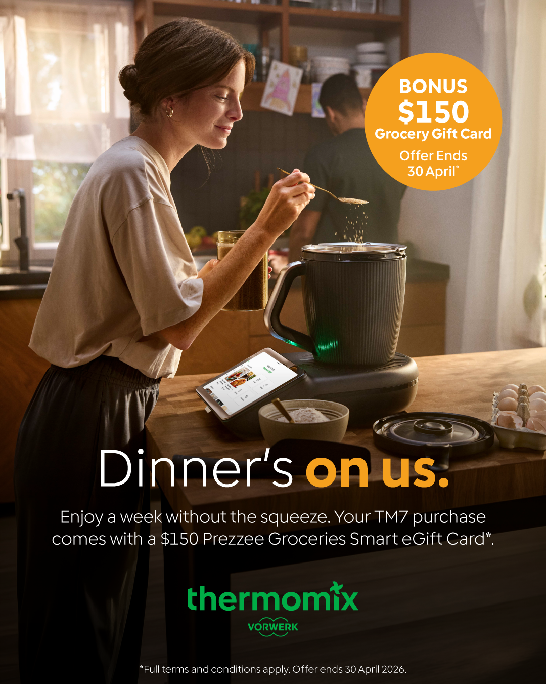 Woman cooking in a kitchen with a Thermomix device on the table. There is a bonus promotion for a $150 grocery gift card ending April 30th.