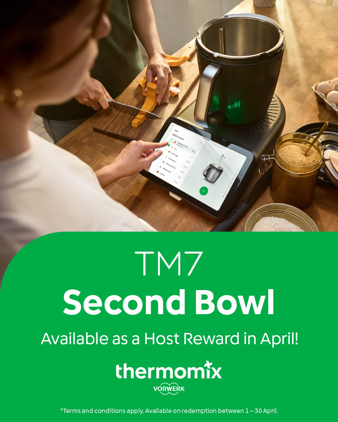 A person chopping pumpkin on a cutting board, while another person uses a tablet with a Thermomix app. The table has various ingredients, a jar of brown sugar, eggs, and a Thermomix appliance.