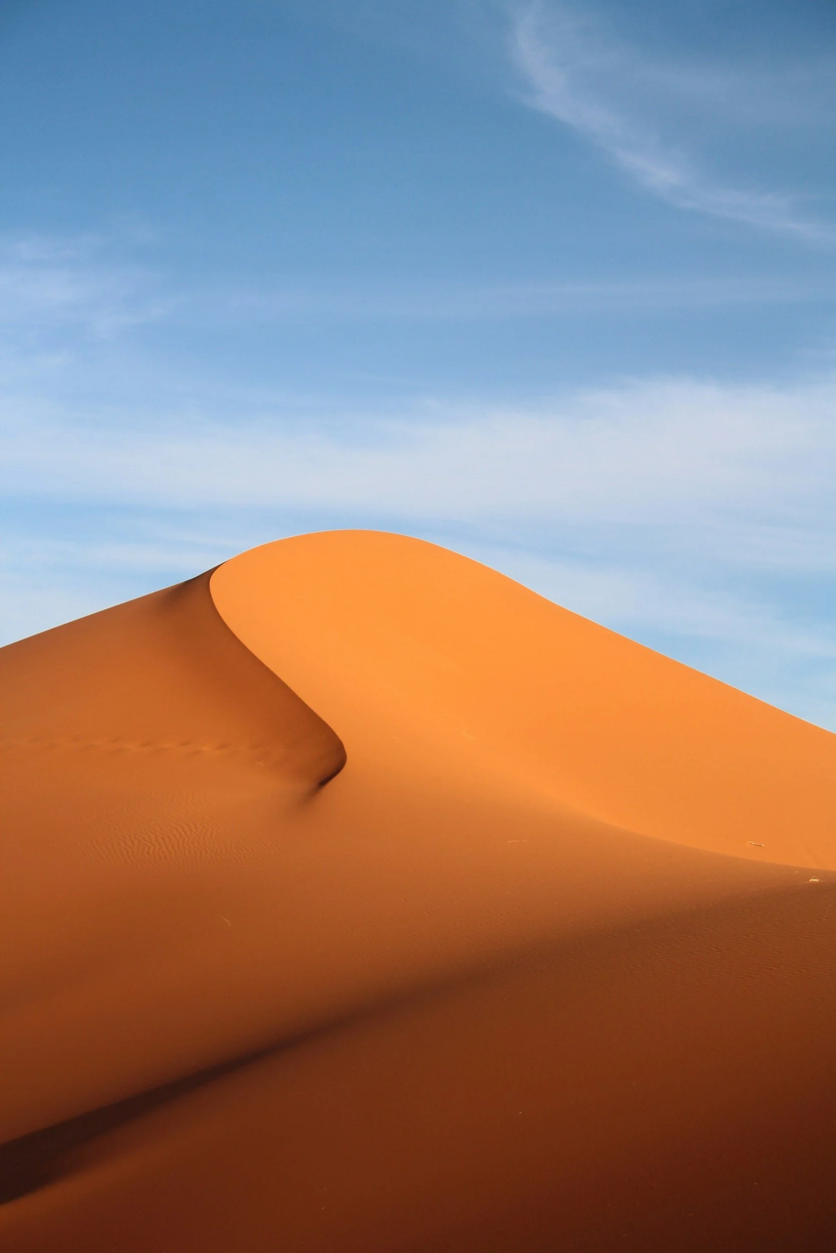 A large orange sand dune against a blue sky with wispy clouds.