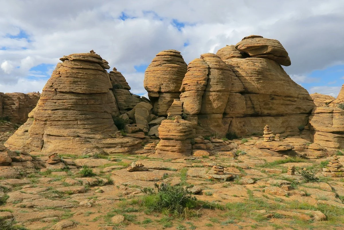 Rock formations and stacked stones in a desert landscape with a cloudy sky.